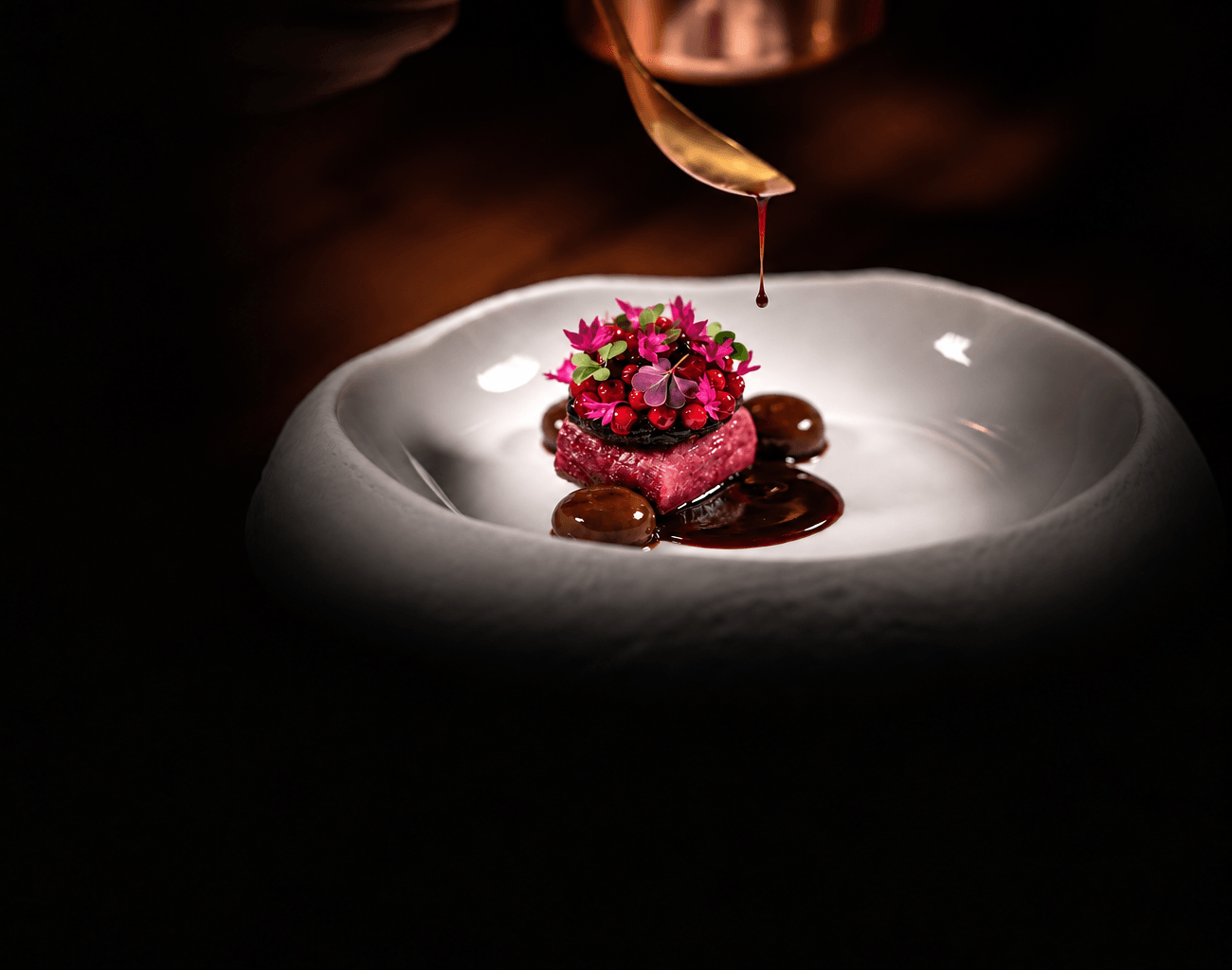 Gericht im MOYA: Sauce wird über ein Stück Fleisch mit Beeren und Blüten in einer weißen Schale abgeschmeckt.